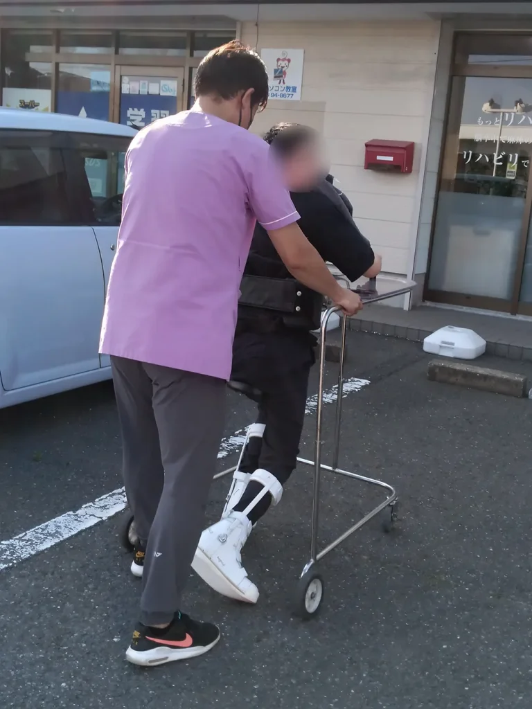 屋外で歩行器を使って歩く練習をするA様と担当者